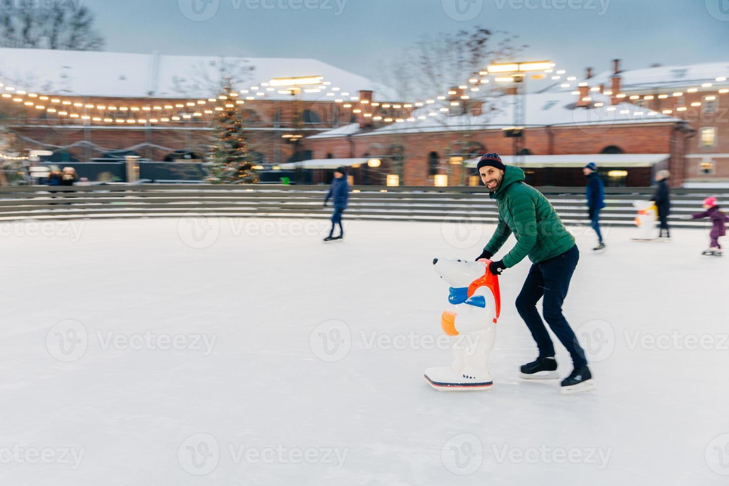 menschen, ferien, winter, freizeitkonzept. Der glückliche bärtige männliche Skater verbringt den Samstag auf der Eisbahn, übt und lernt neue Tricks, unterhält sich und ist in guter festlicher Stimmung. foto