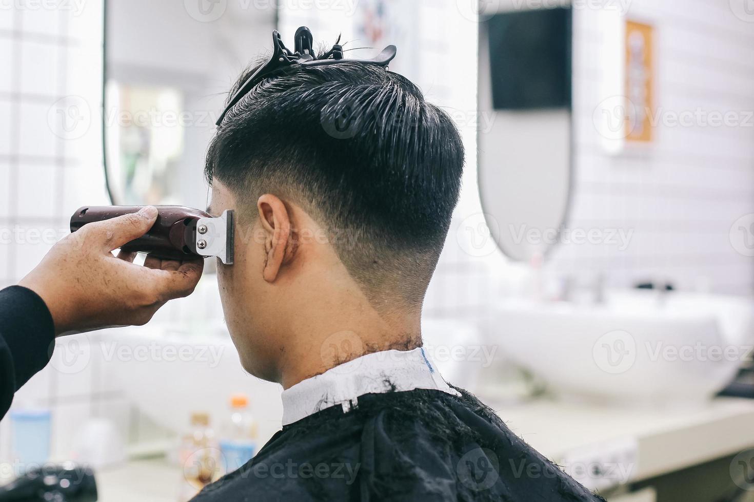 Rückansicht des Friseurs, der die Haare des Verbrauchers mit einer Haarschneidemaschine rasiert. foto