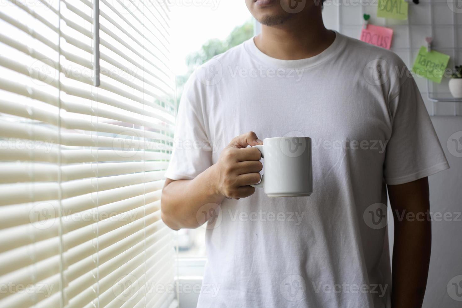 asiatischer mann im weißen hemd, das weißen becher für mock-up hält foto