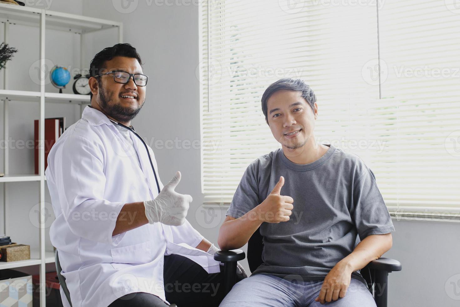 lächelnder arzt und patient sitzen nebeneinander mit daumen hoch geste beim blick in die kamera foto