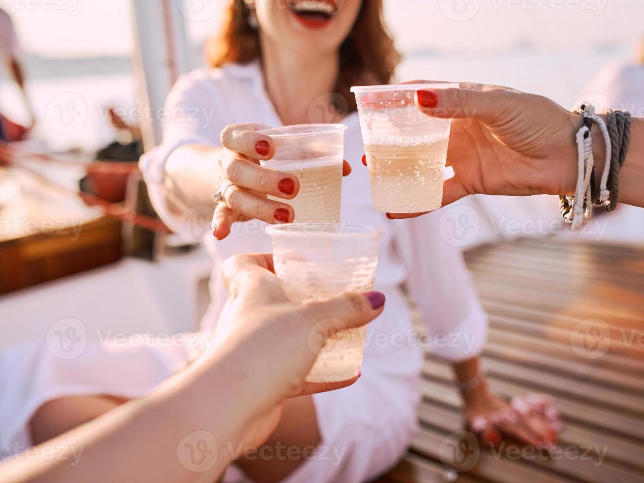 junge frauen halten plastikgläser mit sekt während der reise auf der yacht. Plastik, Umwelt, Recycling, Toast, Partykonzept foto