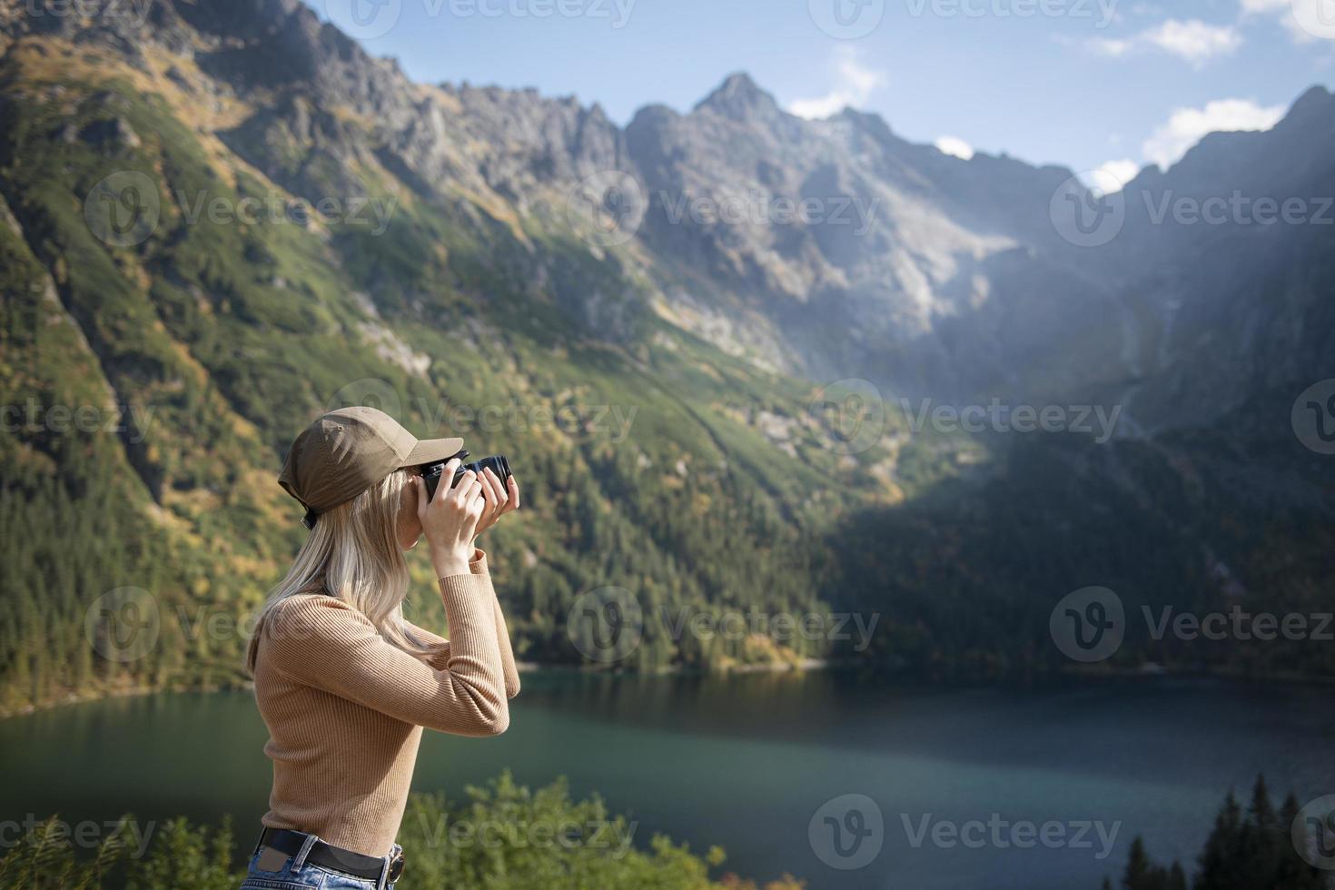 fotograf tourist reisender steht auf grüner spitze auf berg und hält in den händen digitalfotokamera foto