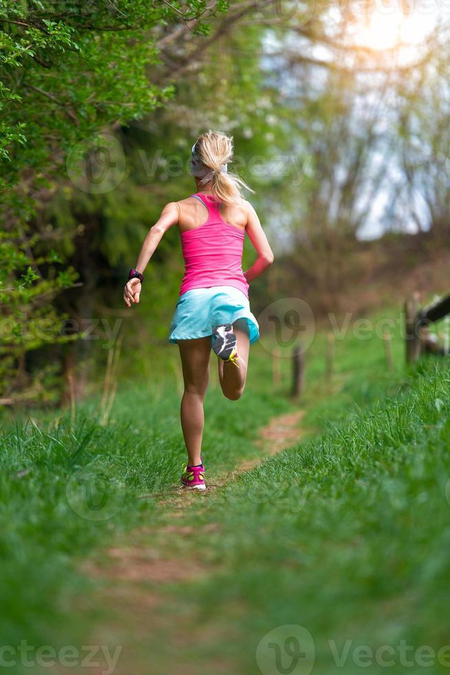 Blonde Sportlerin läuft auf einem Trail in den Wald foto