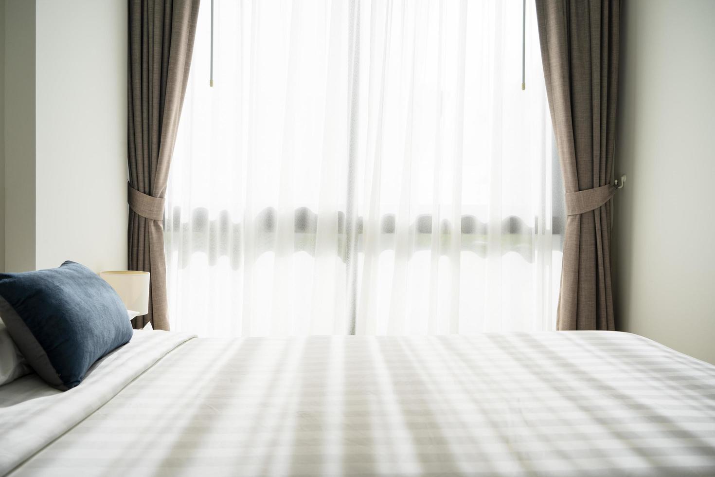 ein Bett mit Kissen und Decken in einem Hotelzimmer mit Vorhängen und Tageslicht von der Sonne. foto