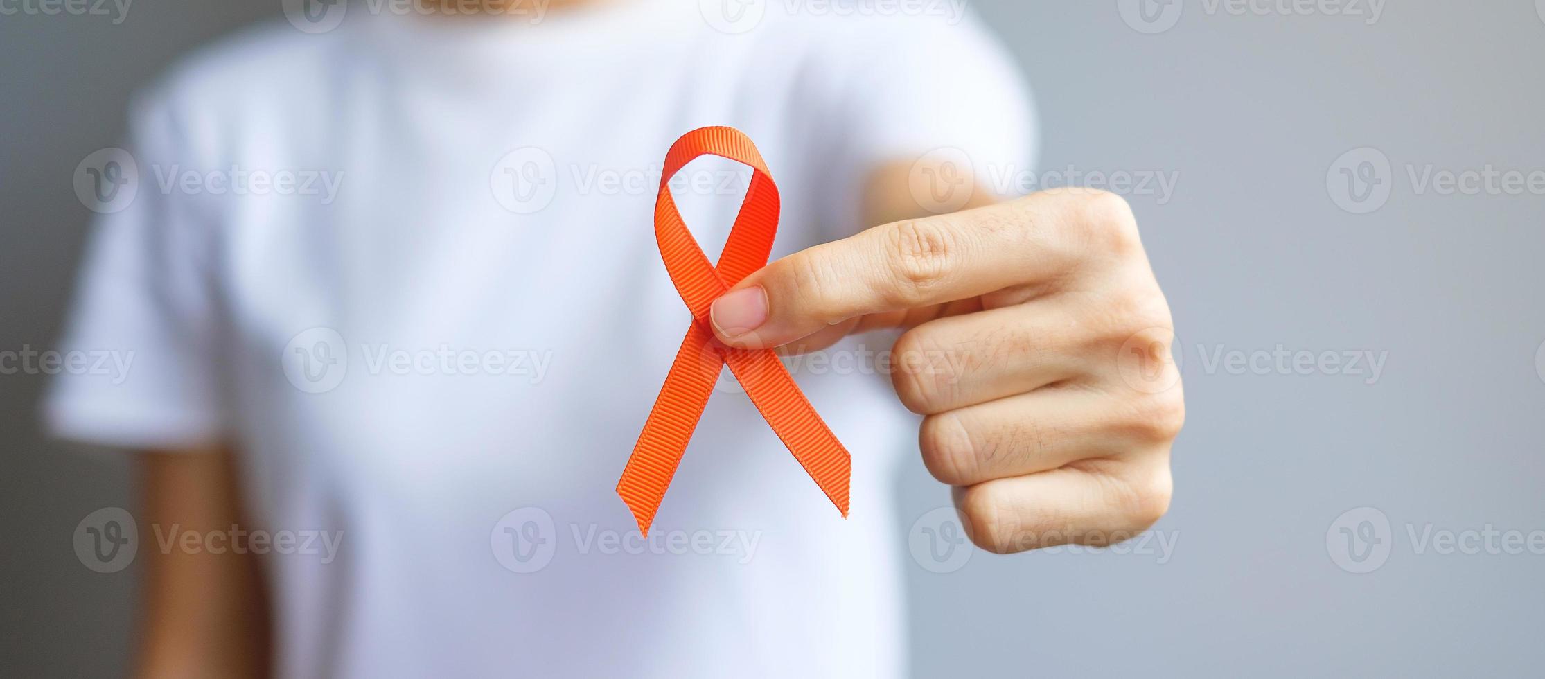 Hand mit orangefarbenem Band für Leukämie, Tag des Nierenkrebses, weltweite Multiple Sklerose, crps, Monat des Bewusstseins für Selbstverletzungen. gesundheits- und wortkrebstageskonzept foto