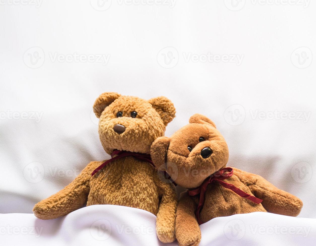 Teddybärpuppe, die im weißen Bett liegt foto