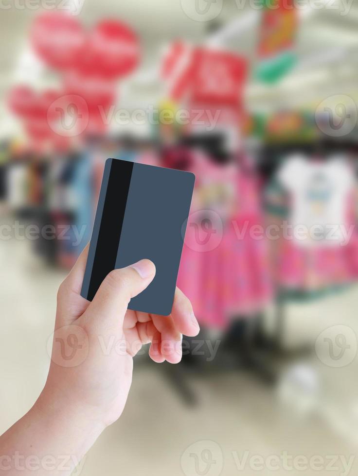 Hand, die Kreditkarte mit unscharfem Hintergrund des Bekleidungsgeschäfts hält foto