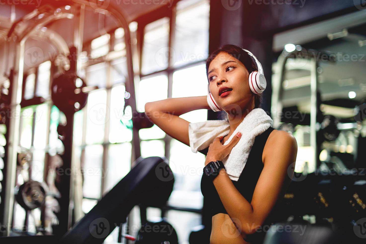 Mädchen im Fitnessstudio, das mit einem Mobiltelefon trainiert, Musik mit weißen Over-Ear-Kopfhörern hört und einen digitalen Herzschlag-Timer verwendet. systematisch ihre Urlaubsentspannung ausüben foto