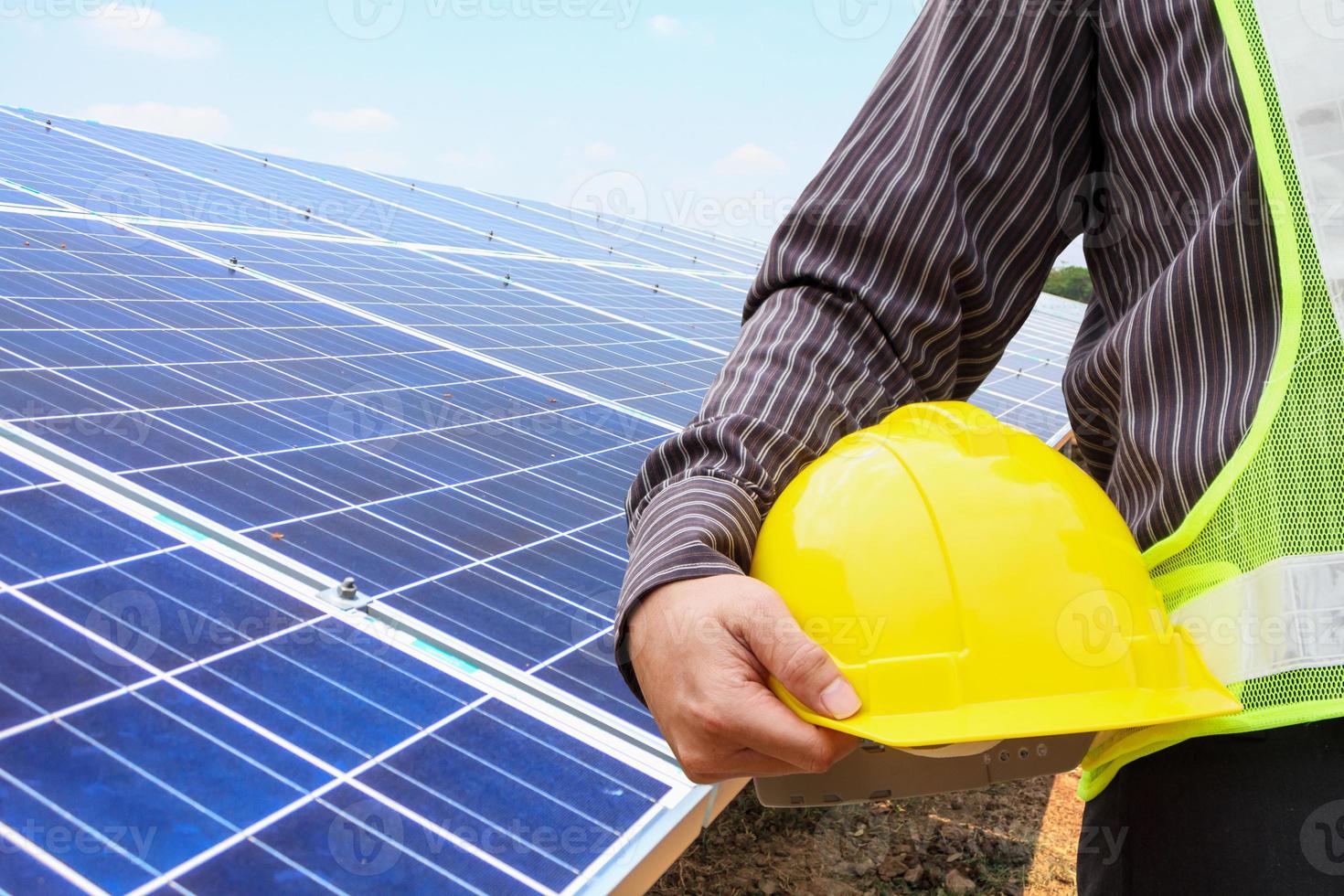 Junger Geschäftsmann-Ingenieur hält gelben Helm am Baustellenhintergrund des Solarpanel-Kraftwerks foto