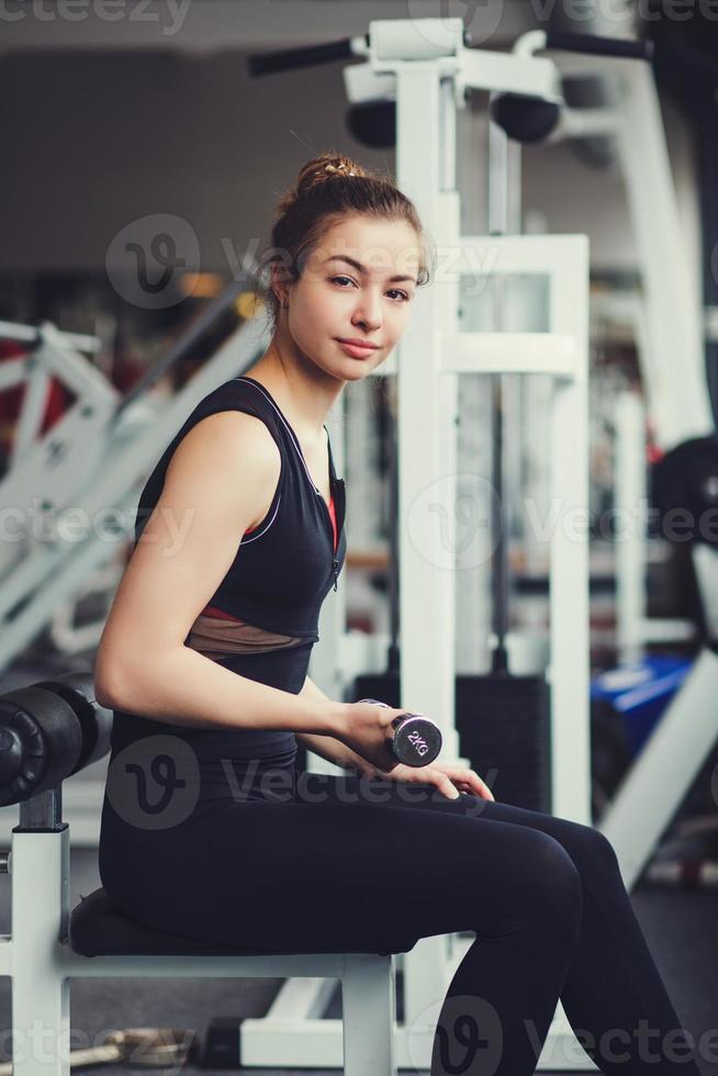 Mädchen nimmt Hanteln im Fitnessstudio auf foto