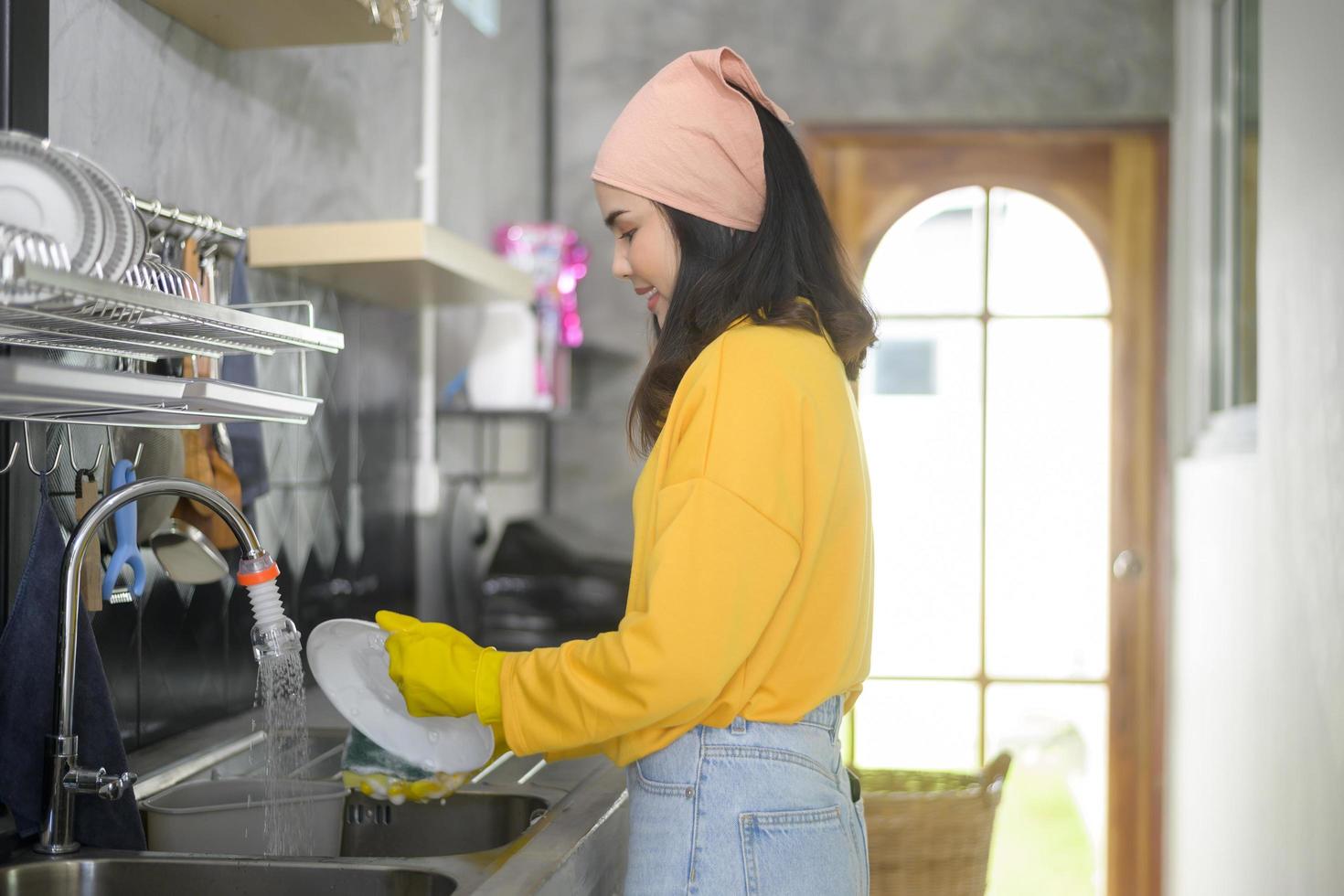 Junge glückliche Frau mit gelben Handschuhen beim Abwasch in der Küche zu Hause foto