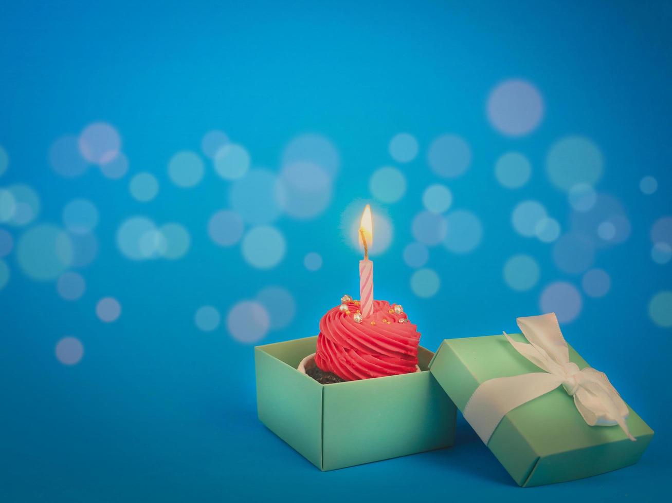 süßer roter Cupcake mit Bogenkerze in Geschenkbox auf blauem Hintergrund mit Kopierraum. alles gute zum geburtstag party konzept hintergrund. foto