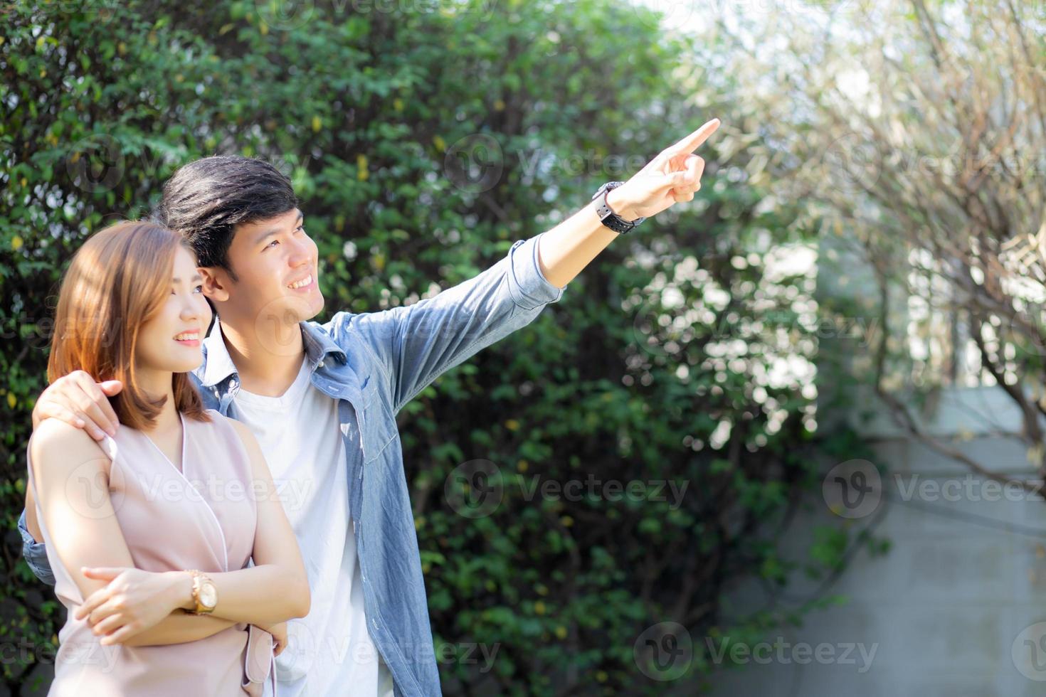 schönes porträtpaar, das sich gegenseitig die augen ansieht und mit einer glücklichen, jungen asiatischen beziehung zwischen mann und frau lächelt, die auf etwas zeigt, gefühl und emotion von ehemann und ehefrau, liebhaber und lebensstilkonzept. foto