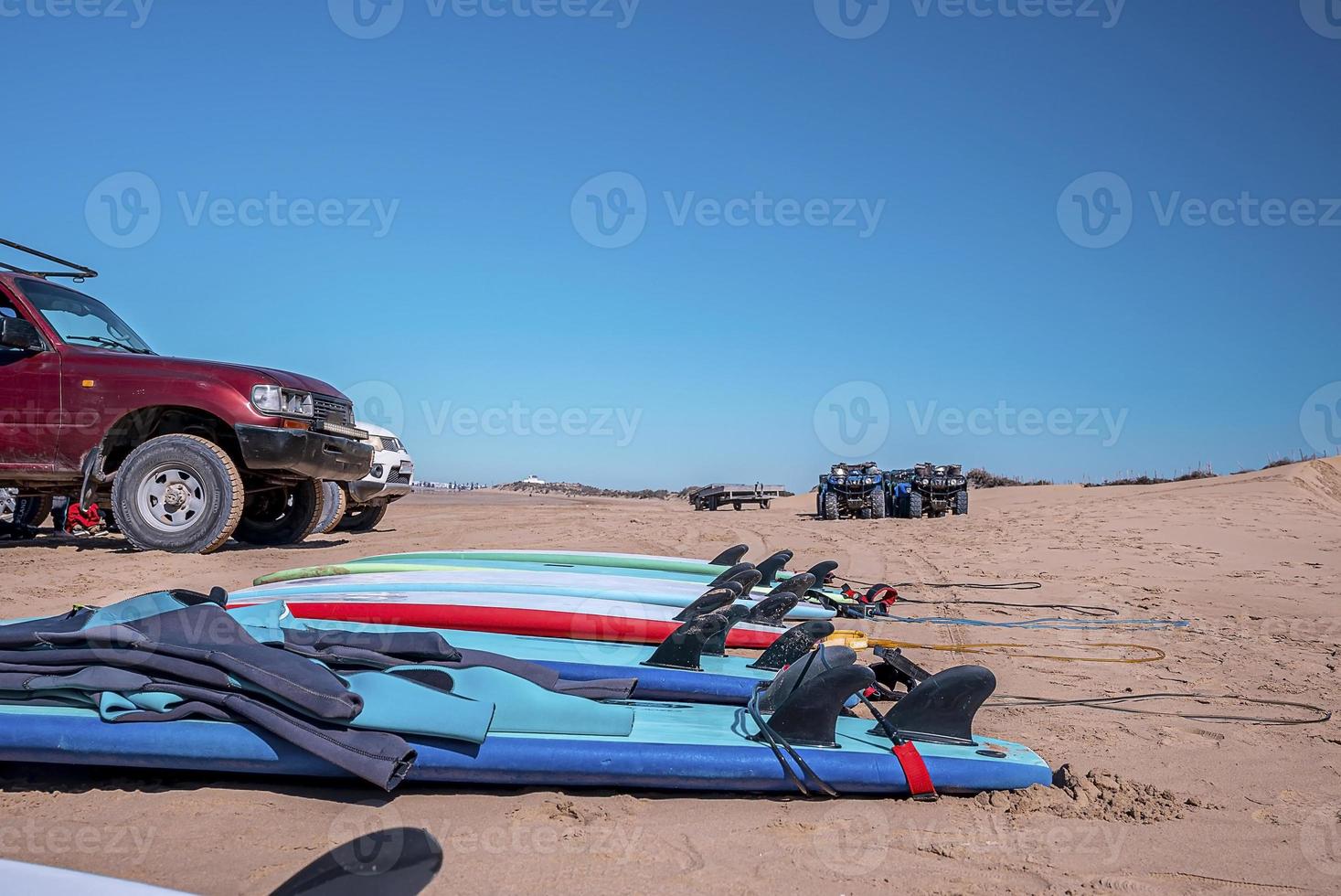 Surfbretter mit Taucheranzügen, die am Strand vor blauem Himmel auf Sand legen foto