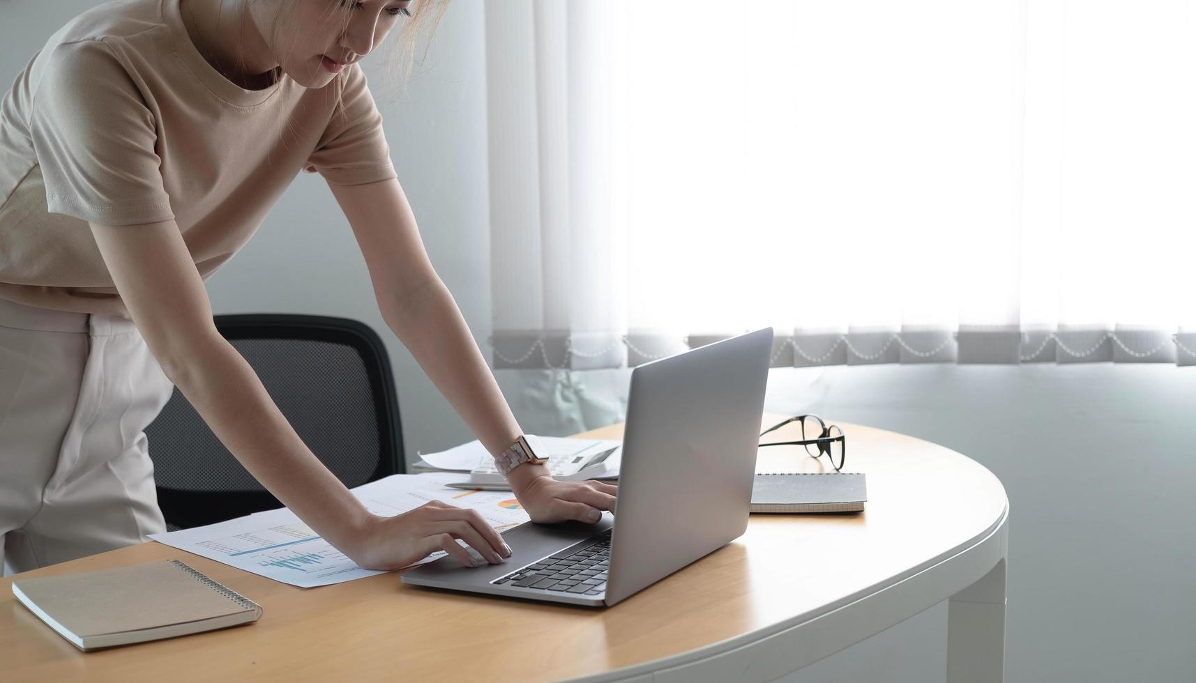 Attraktive junge brünette Asiatin mit Laptop-Computer, während sie in einem stilvollen Büroraum steht. foto