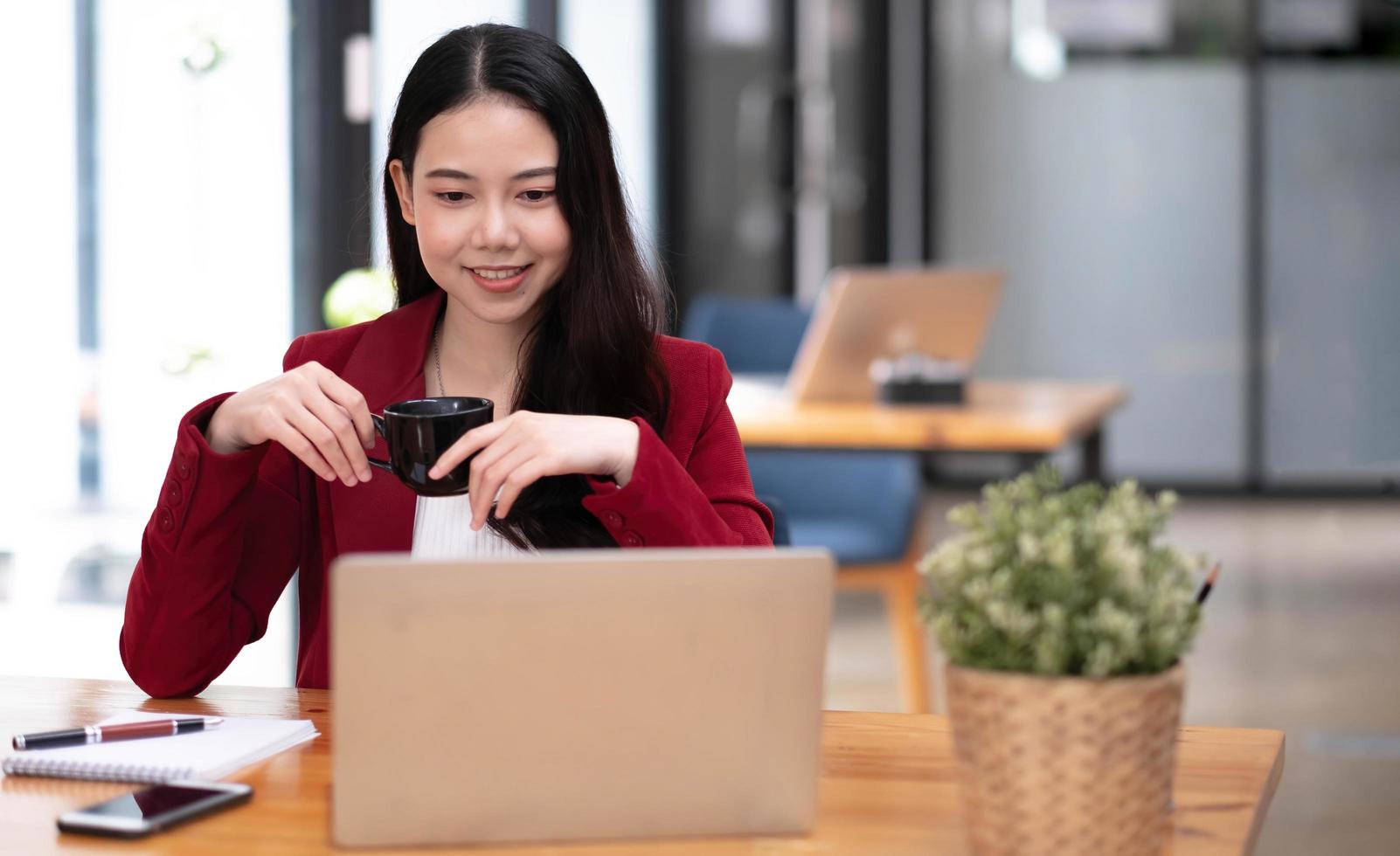 junge asiatische geschäftsfrau hat das vergnügen, die arbeit auf ihrem tablet und ihrem lieblingskaffee im büro zu beobachten. foto