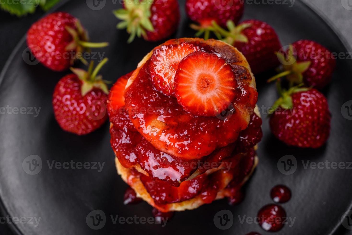 Quarkpfannkuchen mit geschnittenen Erdbeeren und Erdbeermarmelade auf einem Teller auf Betongrund foto