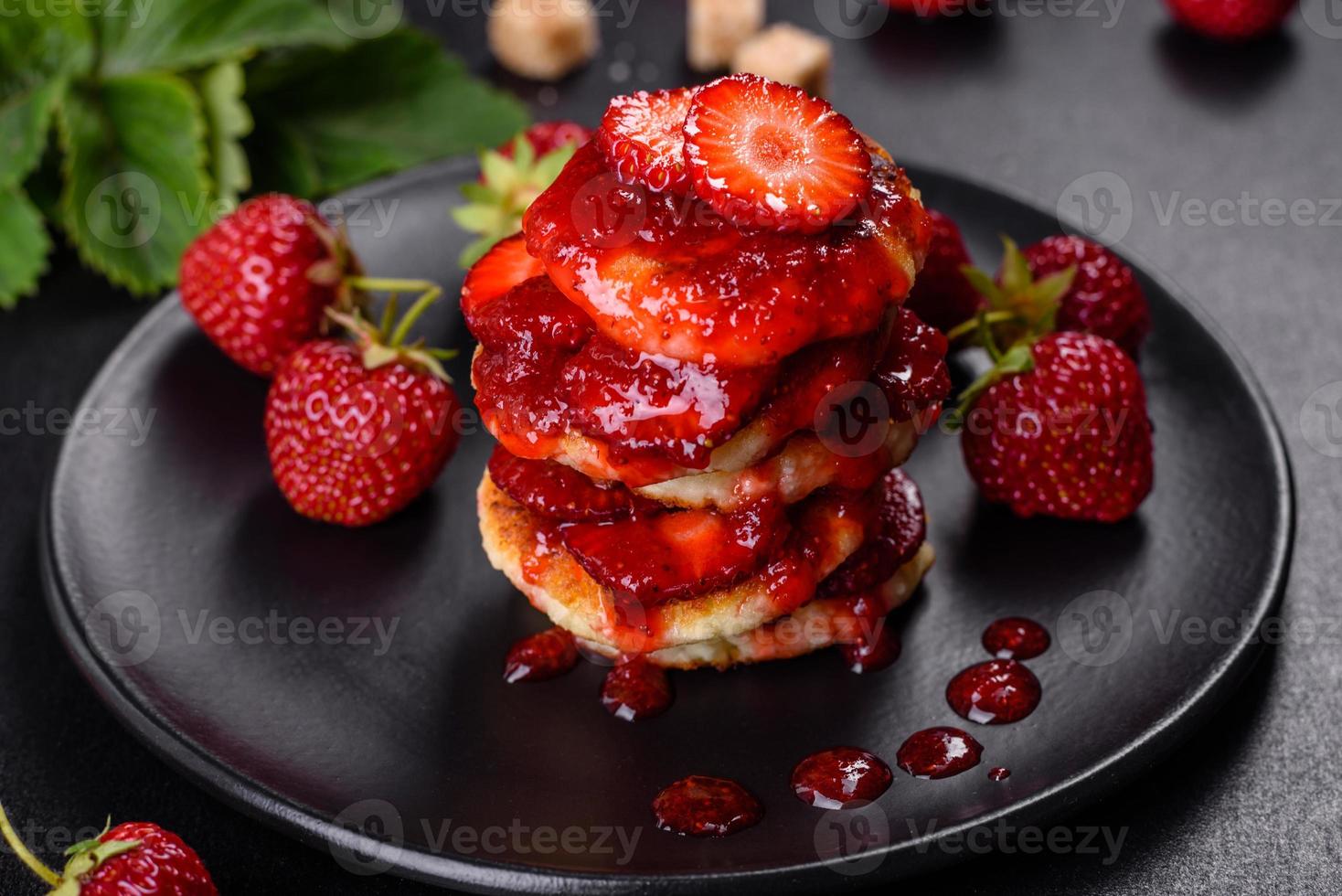Quarkpfannkuchen mit geschnittenen Erdbeeren und Erdbeermarmelade auf einem Teller auf Betongrund foto