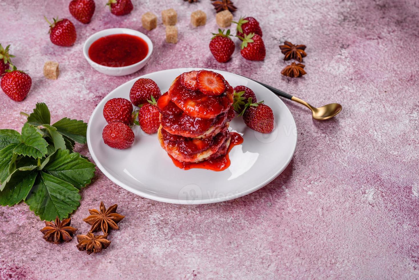 Quarkpfannkuchen mit geschnittenen Erdbeeren und Erdbeermarmelade auf einem Teller auf Betongrund foto