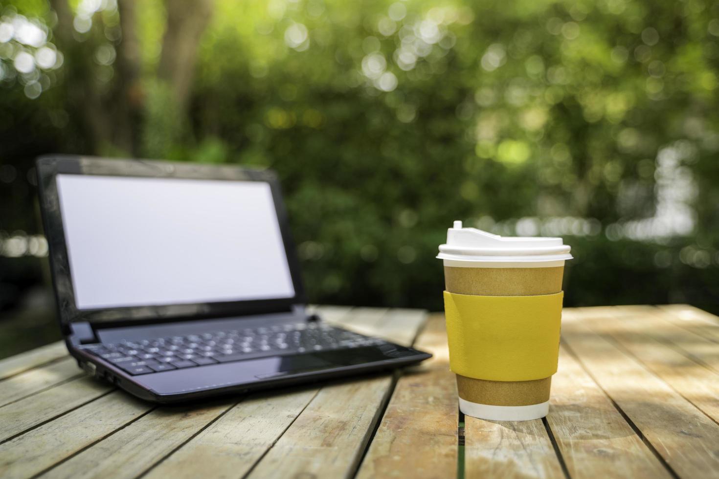 Kaffeetassenpapier mit einem Computerlaptop im grünen Naturhintergrund. remote oder von zu Hause aus arbeiten. weicher Fokus. flacher Fokuseffekt. foto