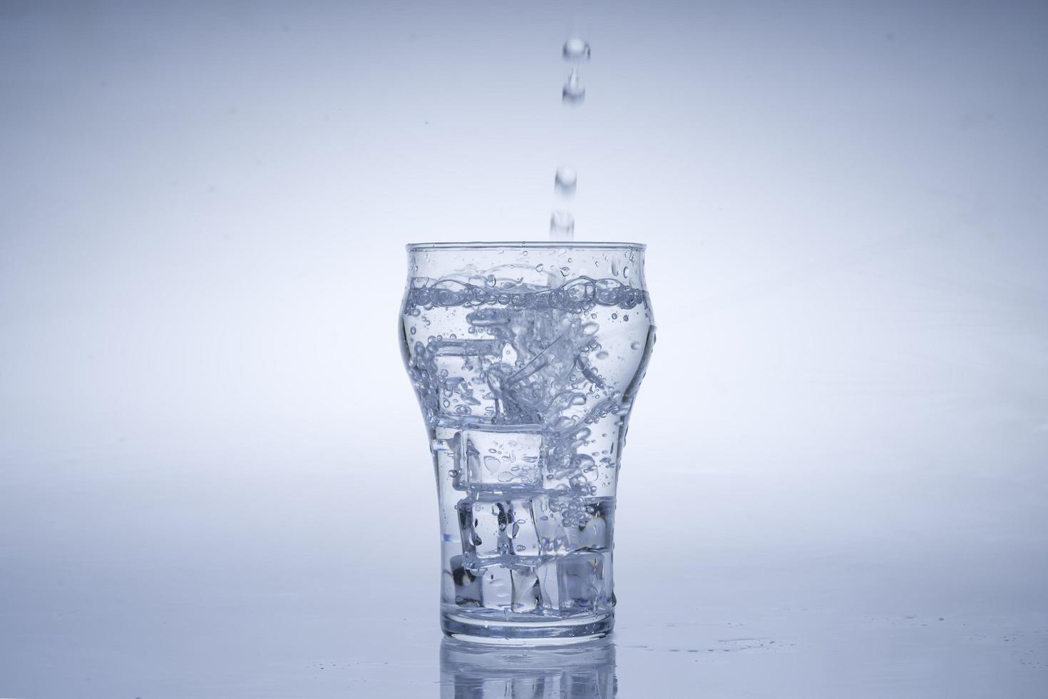 Eiswürfel fiel in das Wasserglas. Wasser spritzte aus dem klaren Glas. frisches Konzept foto