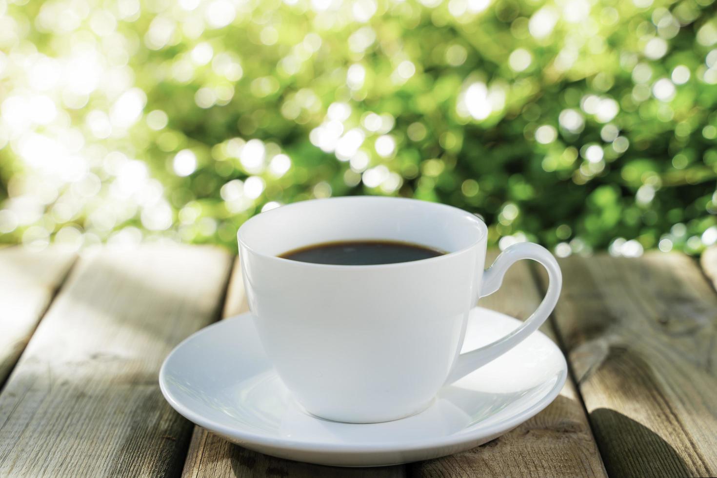 weiße keramikkaffeetasse auf dem holzboden, grüner baum bokeh hintergrund. weicher Fokus. flacher Fokuseffekt. foto