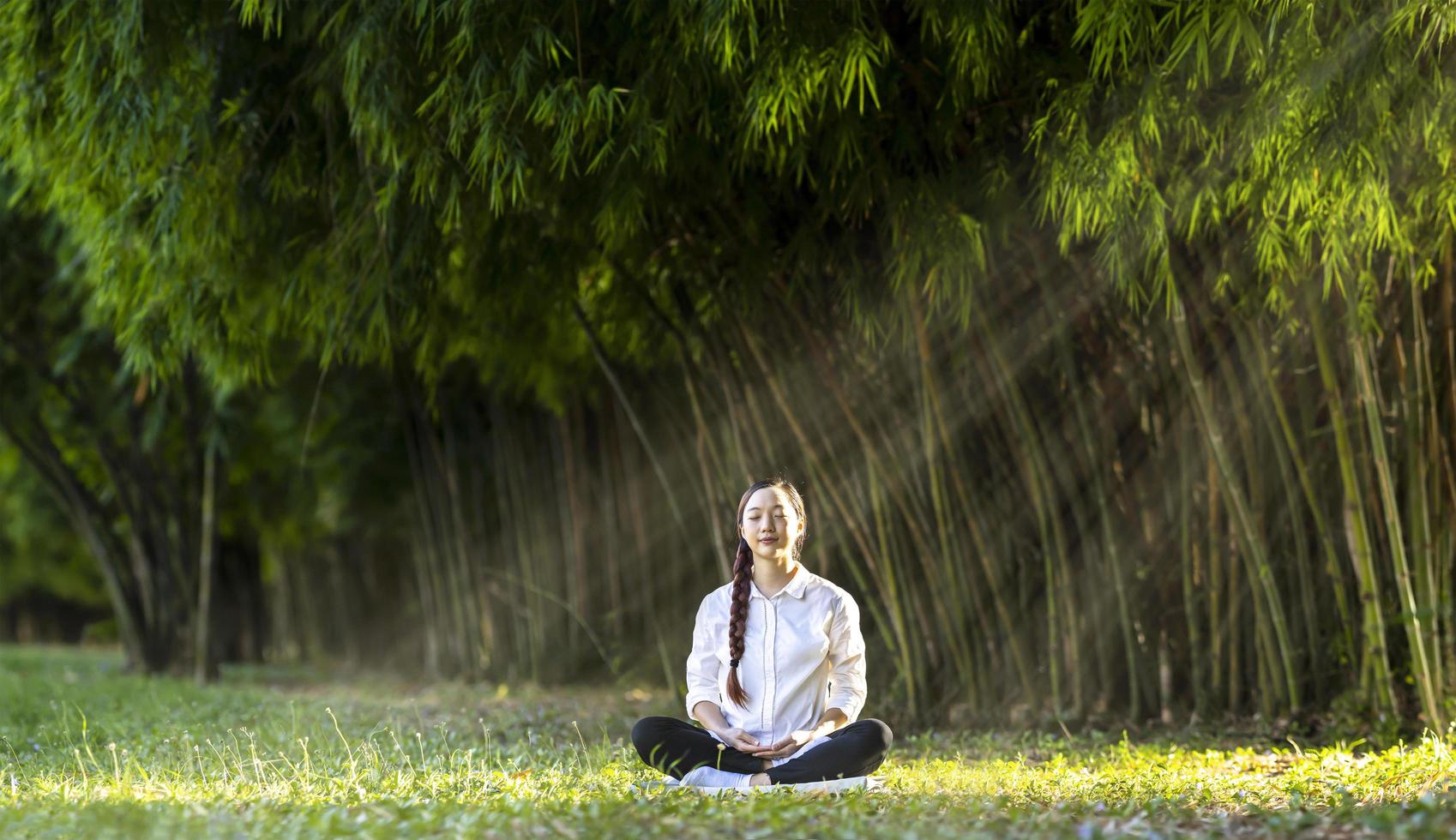 Frau, die entspannend Meditation im Bambuswald praktiziert, um Glück aus innerer Friedensweisheit für ein gesundes Wellness-Geist- und Wohlbefinden-Seelenkonzept zu erlangen foto