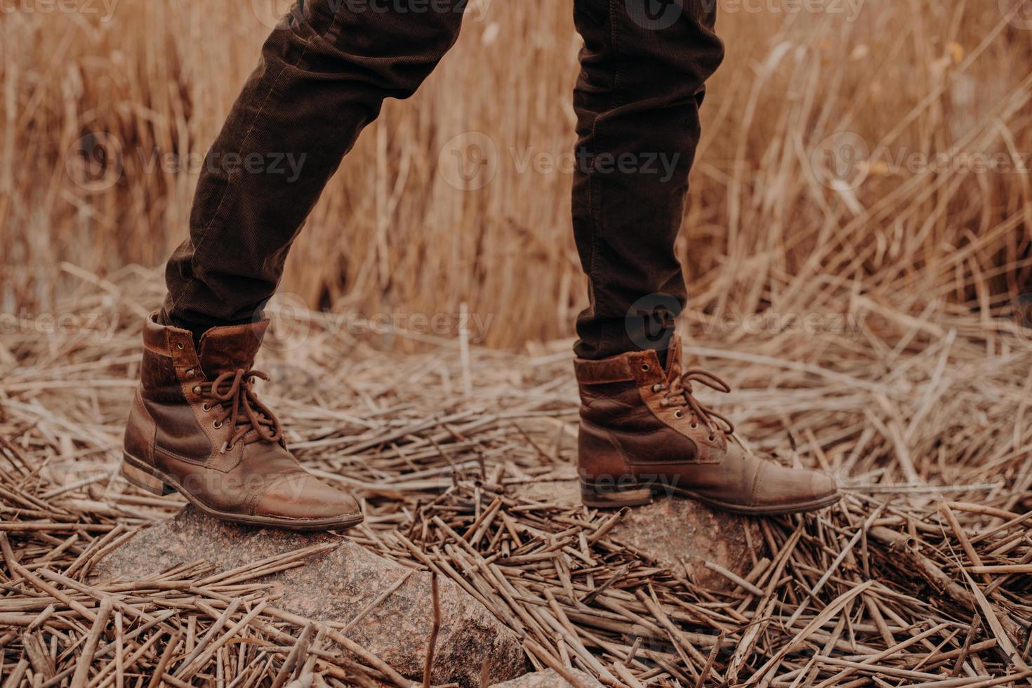 beschnittene aufnahme eines nicht erkennbaren mannes trägt alte lederbraune schuhe, posiert auf dem boden mit stoppeln, geht allein auf dem feld spazieren. foto