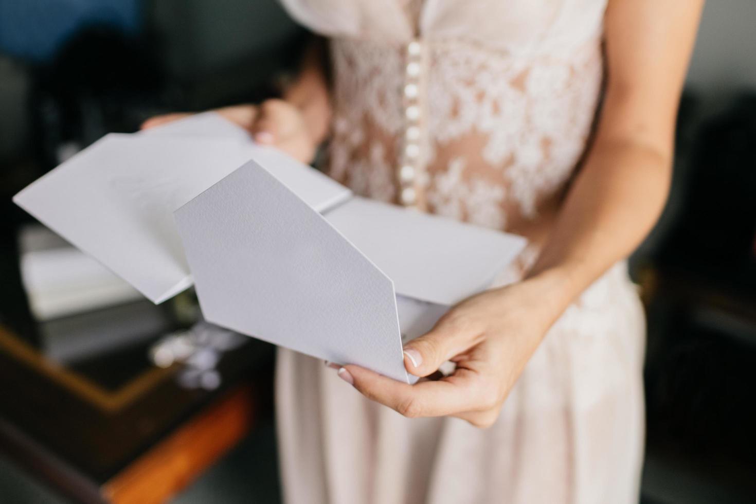 weibliche braut im weißen kleid, hält weißen brief oder umschlag, bereitet sich auf einladung vor, bereitet sich auf hochzeitszeremonie vor. Heiratskonzept foto