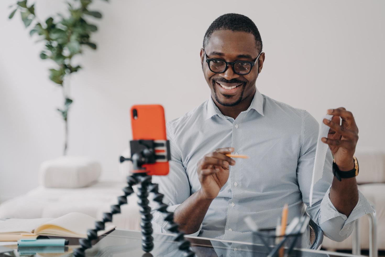 Lächelnder afroamerikanischer Geschäftsmann, der Geschäftsdaten online per Videoanruf mit Smartphone präsentiert foto