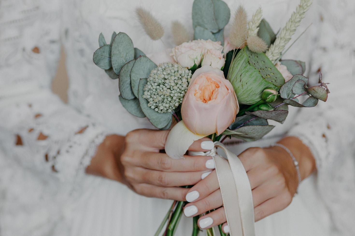 schöne Blumen in den Händen der Braut. Brautstrauß. Frau im weißen Hochzeitskleid für die Hochzeitszeremonie vorbereitet. selektiver Fokus foto