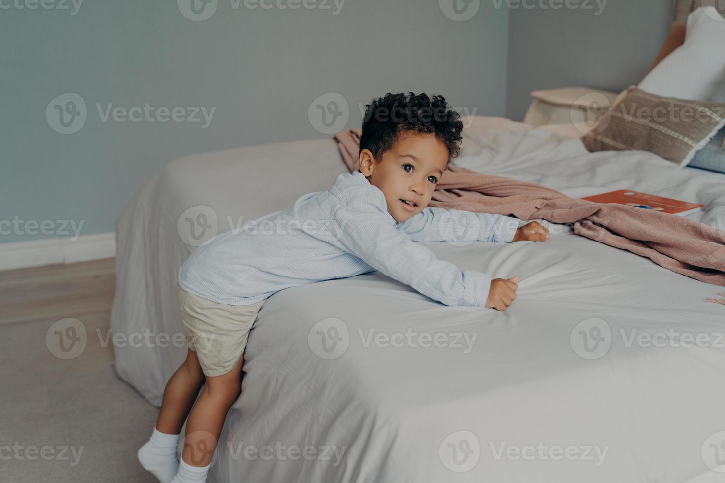 Süßer kleiner afroamerikanischer Junge, der zu Hause im gemütlichen Schlafzimmer spielt foto