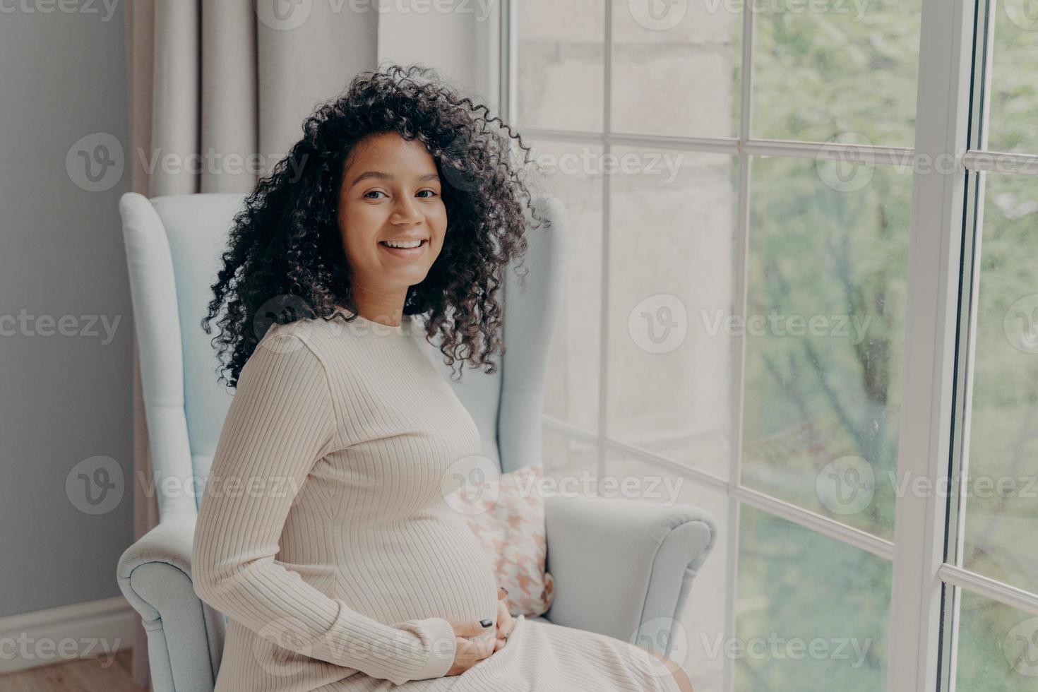 glückliche afroamerikanische frau im weißen kleid, das schwangerschaft genießt foto