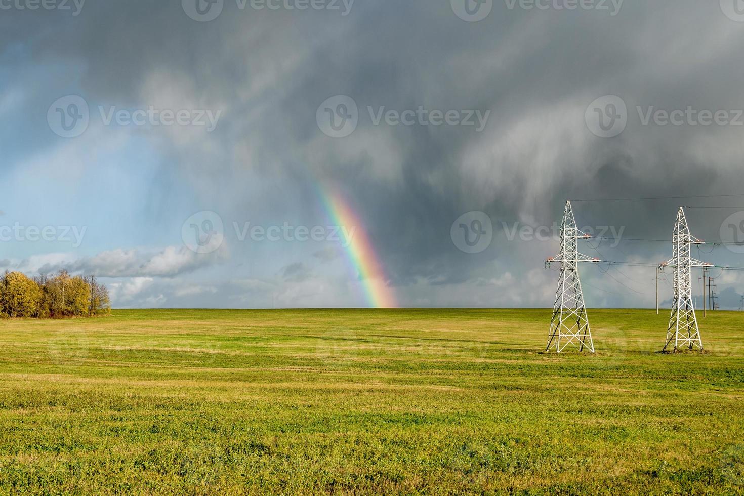 Regenbogen über dem Feld und Hochspannungsmasten foto