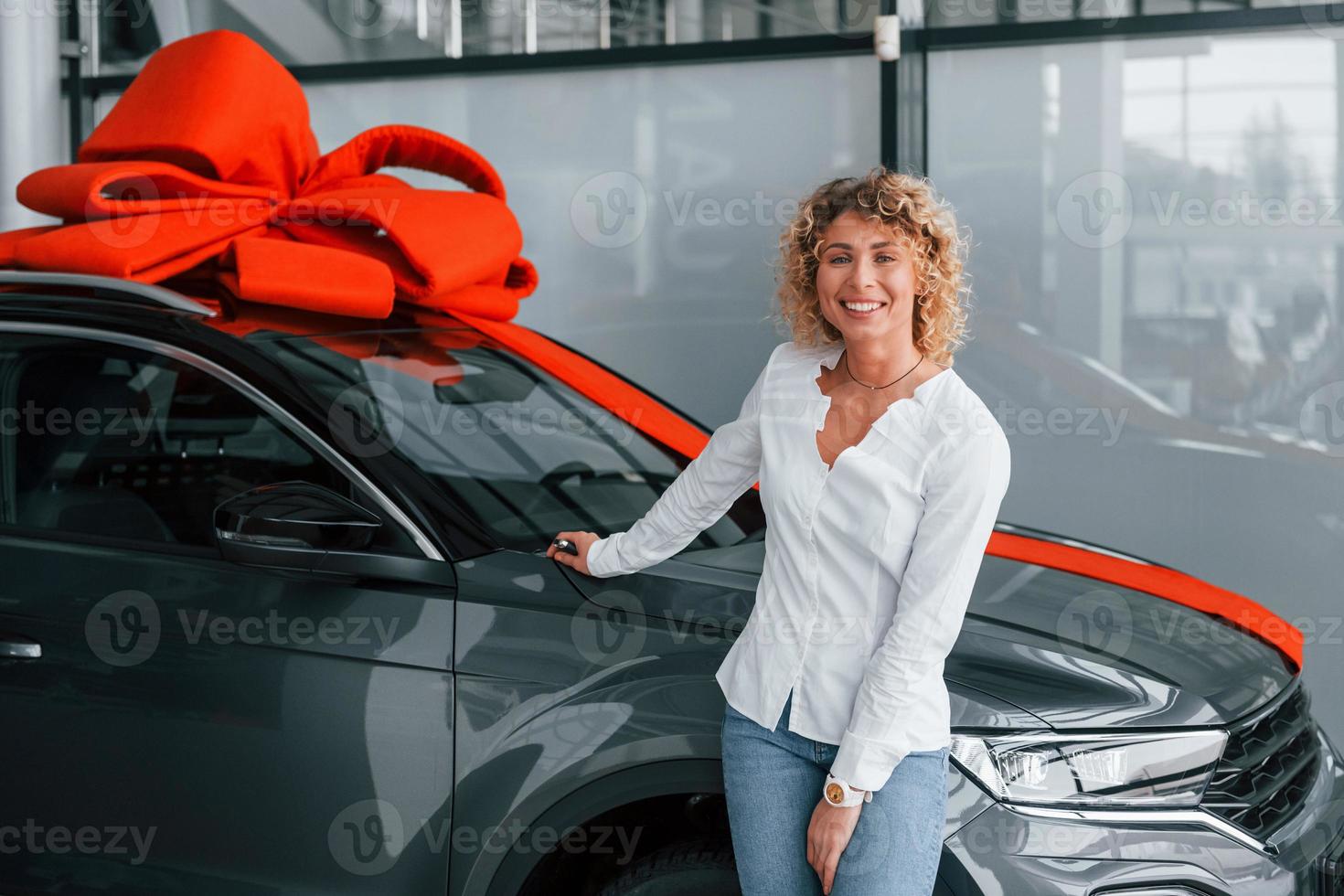 Auto ist oben mit Geschenklänge. frau mit lockigen blonden haaren ist im autosalon foto