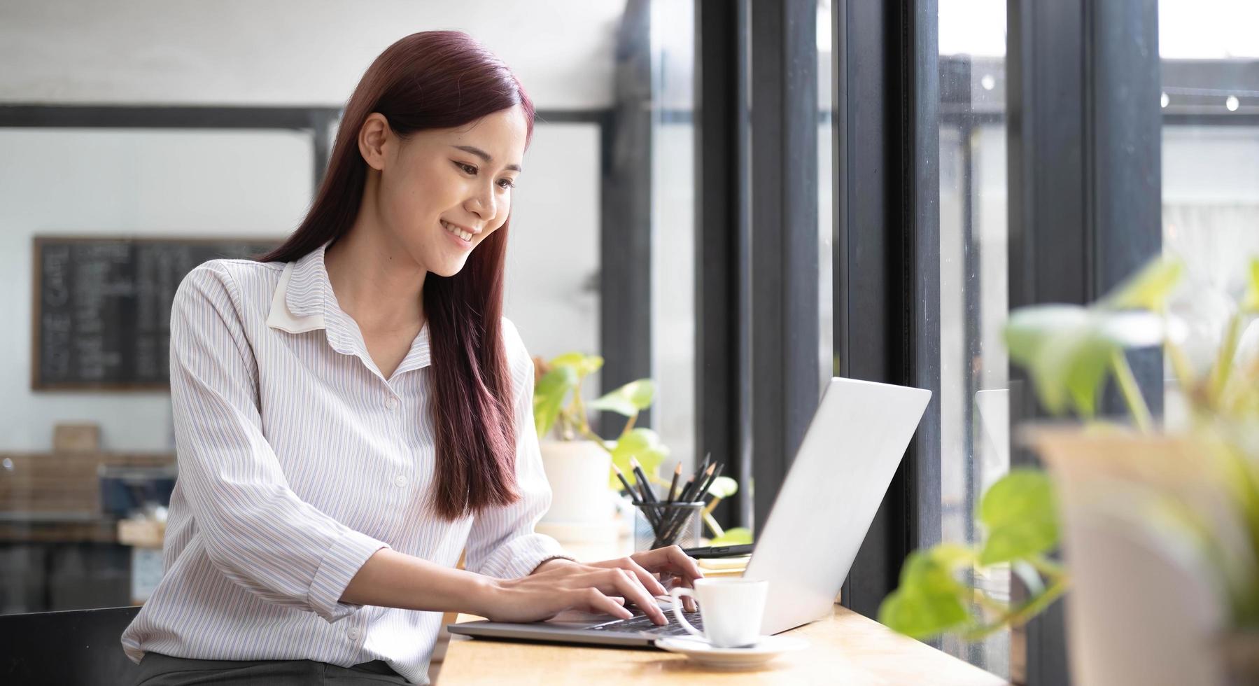 Nahaufnahme Porträt einer schönen jungen asiatischen Frau, die lächelt und auf den Laptop-Bildschirm schaut foto