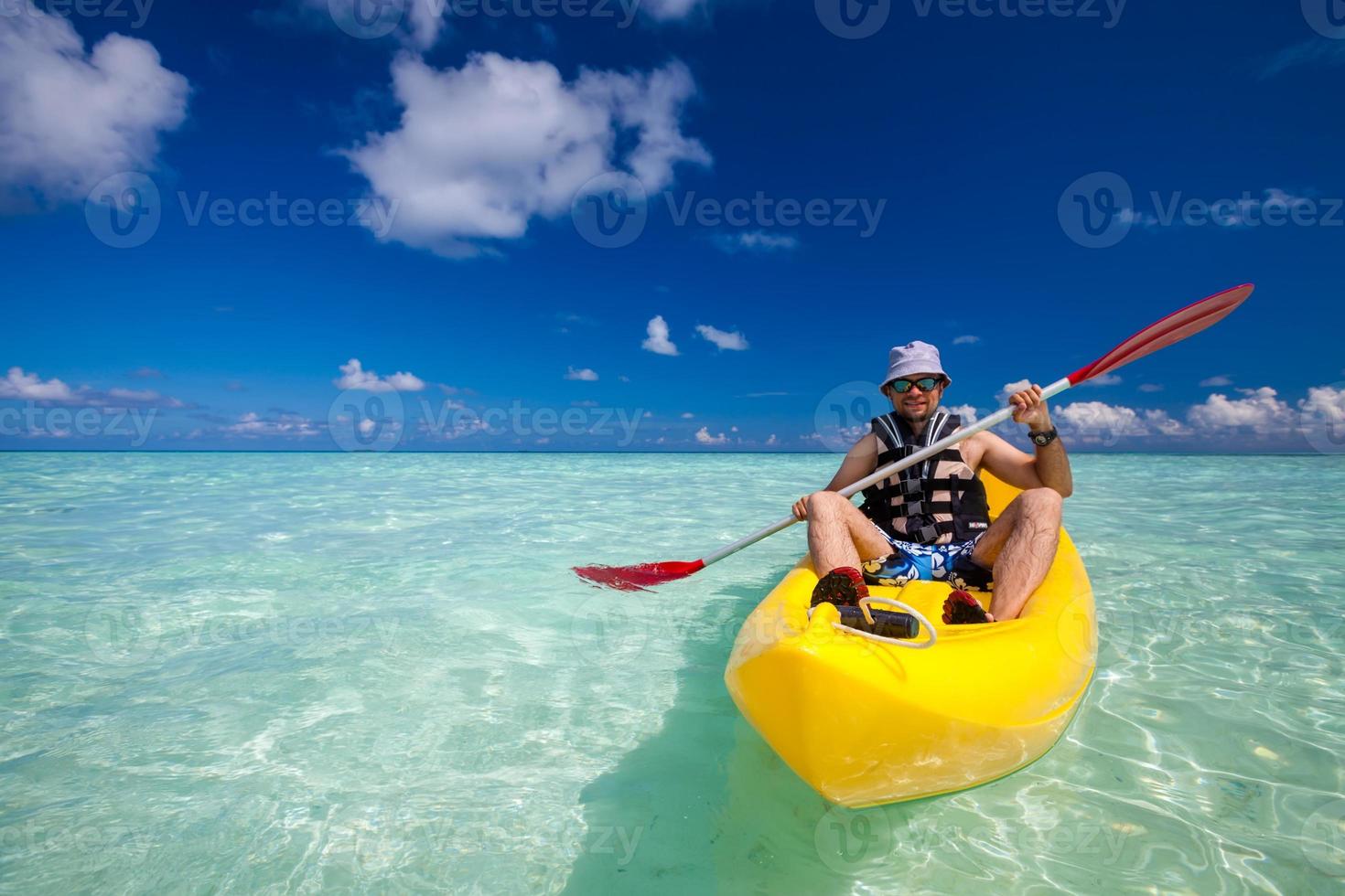 junger kaukasischer Mann, der im Meer auf den Malediven Kajak fährt foto