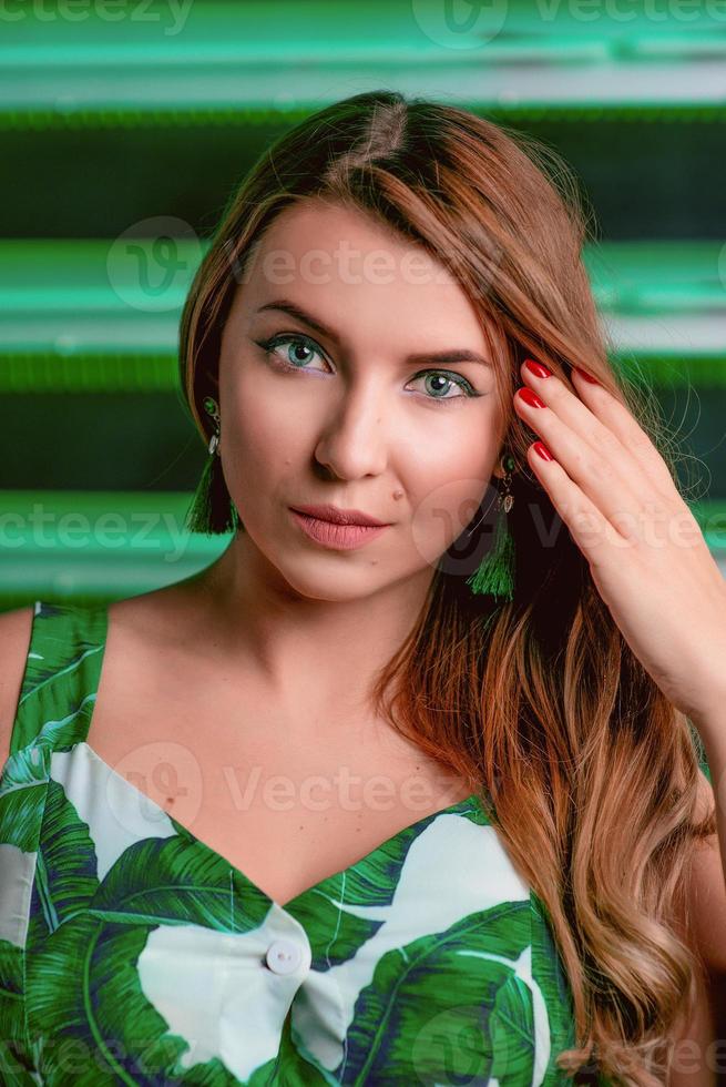 Porträt einer stilvollen Frau mit braunen Haaren in grünem Kleid, grünen Ohrringen, mit Make-up auf grünem Hintergrund im Fotostudio. Weiblichkeit, Weiblichkeit, Reisen, Modekonzept foto
