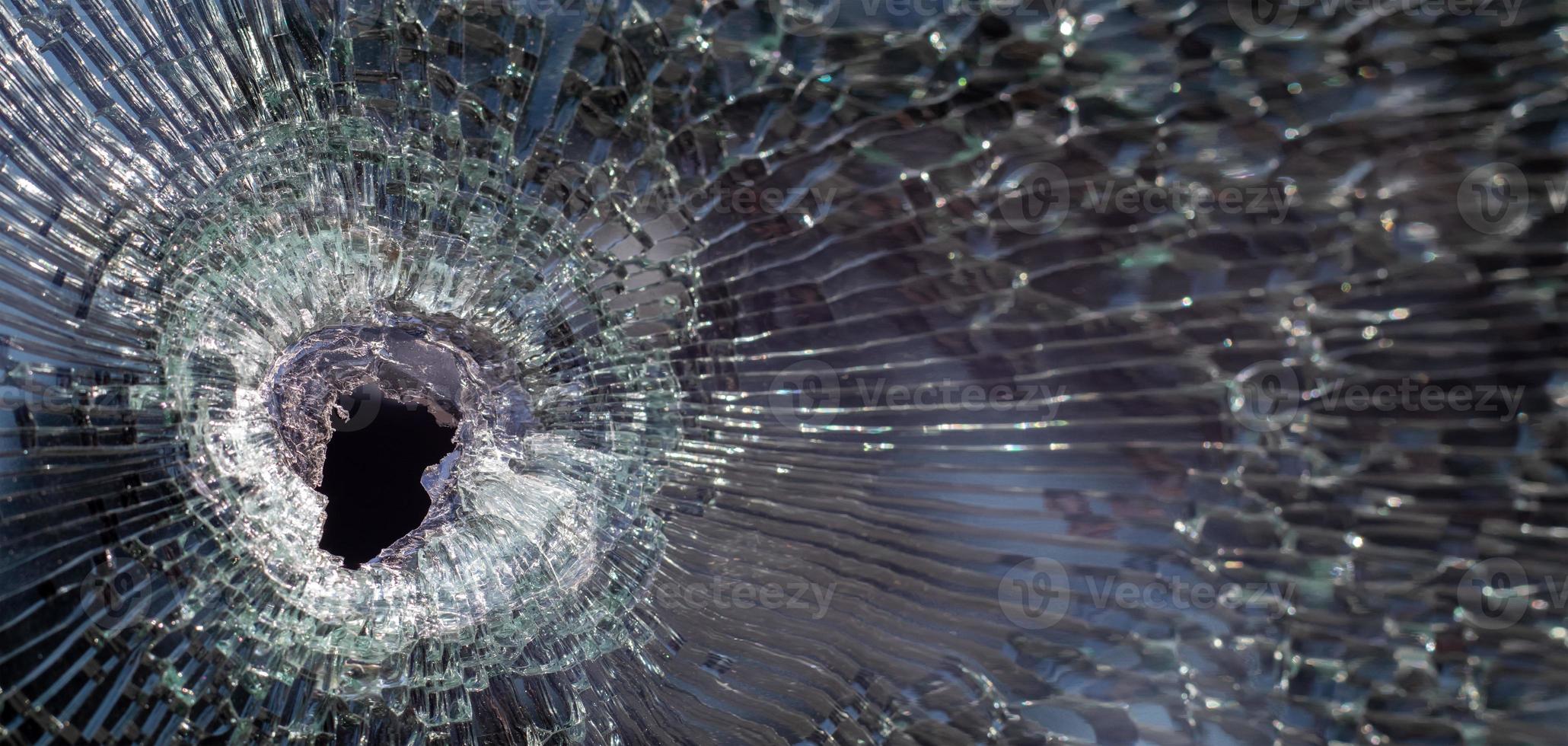 Einschussloch im Glas mit Rissen, echtes Einschussloch aus nächster Nähe. Die Kugel hinterließ ein zerbrochenes Loch in der Windschutzscheibe eines Autos oder ein durch einen Unfall zersplittertes Fensterglas. Banner mit Kopierbereich. foto