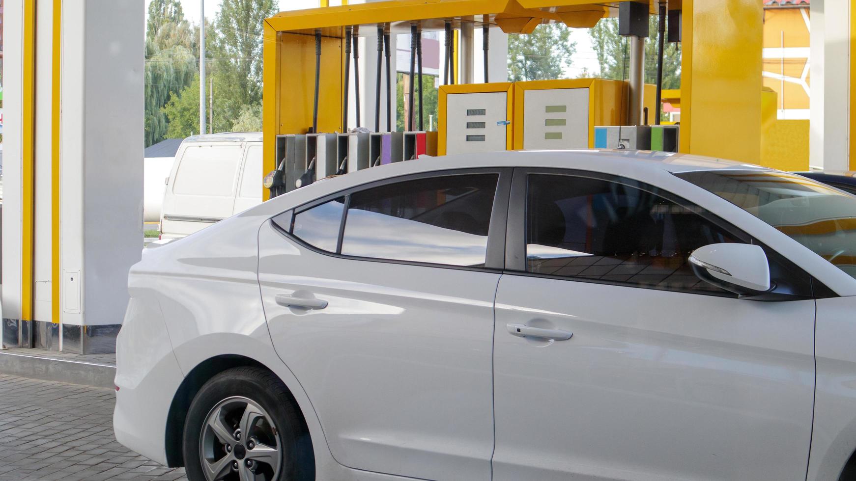Das weiße Auto tankt. Betanken eines an einer Tankstelle geparkten Autos. Autos mit Zapfsäule an Tankstellen betanken. Energie aus Öl und Gas. Treibstoffknappheit in der Ukraine. Bild von Pumpen an einer Tankstelle. foto