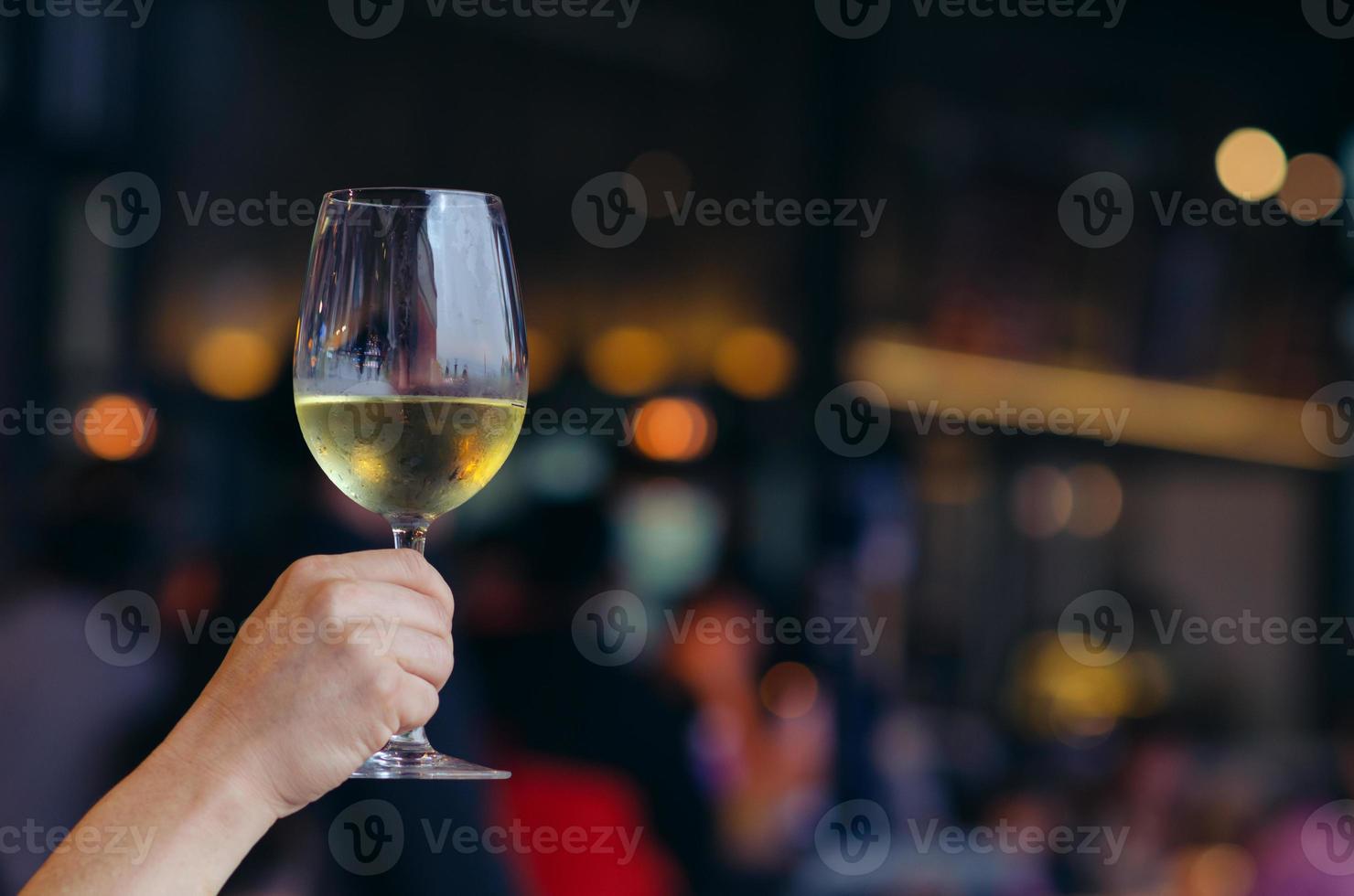 Hand, die ein Glas Weißwein mit buntem Bokeh-Licht im Restaurant hält. foto