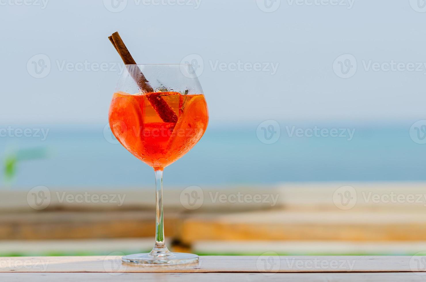 Ein Glas Orangencocktail wird mit verschwommenem Meereshintergrund für Urlaubs- und Sommergetränkekonzept auf den Tisch gestellt. foto