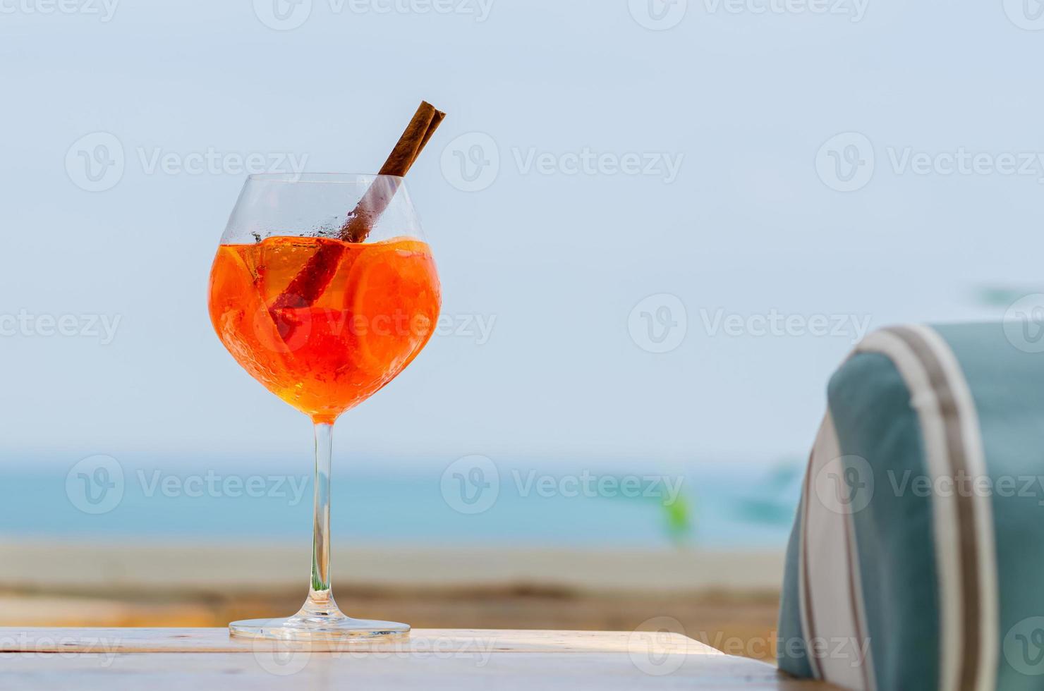 Ein Glas Orangencocktail wird mit verschwommenem Meereshintergrund für Urlaubs- und Sommergetränkekonzept auf den Tisch gestellt. foto