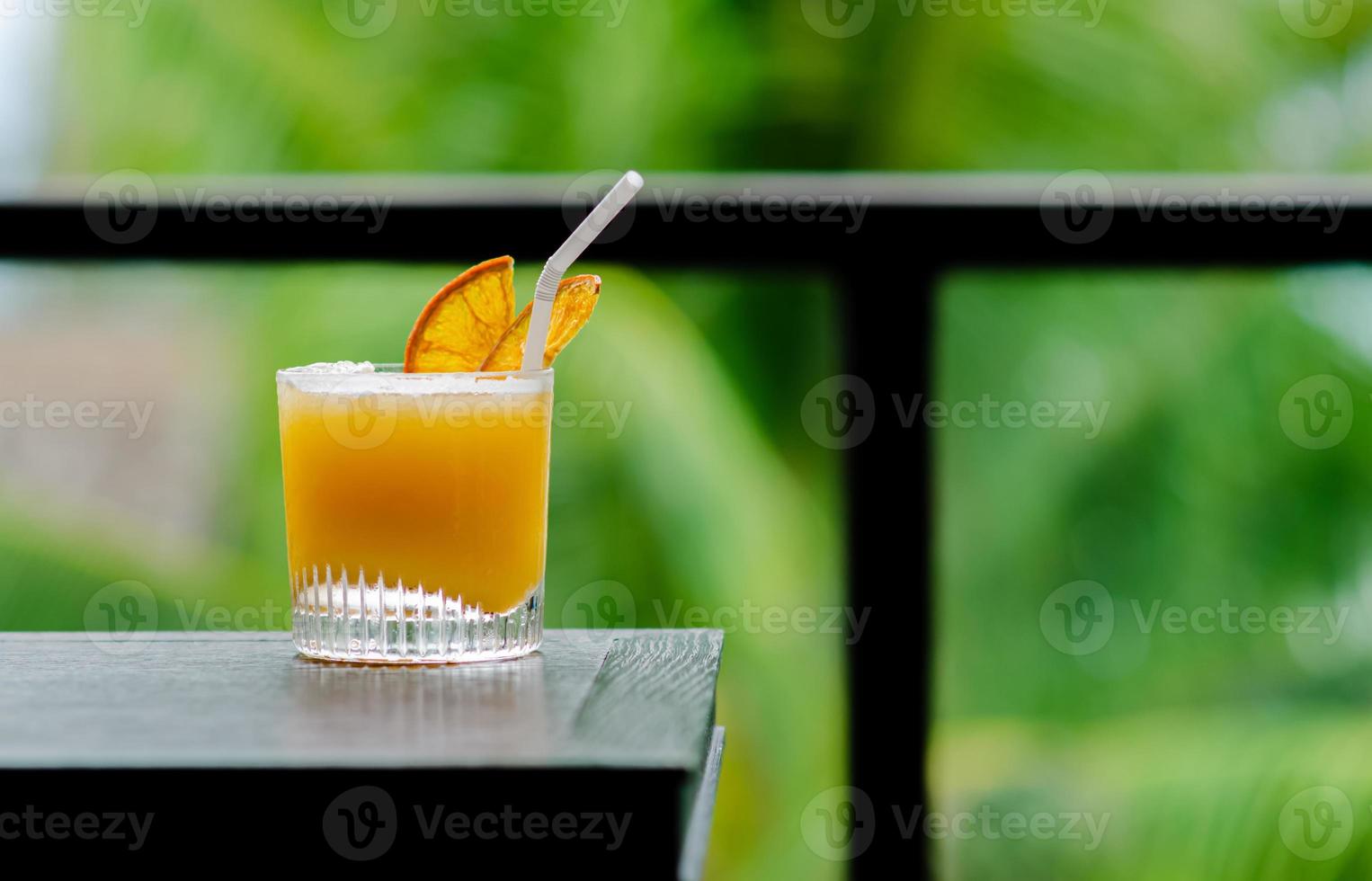 Ein Glas Orangencocktail wird auf den Tisch der Bar mit grünem Hintergrund für Urlaubs- und Sommergetränkekonzept gestellt. foto