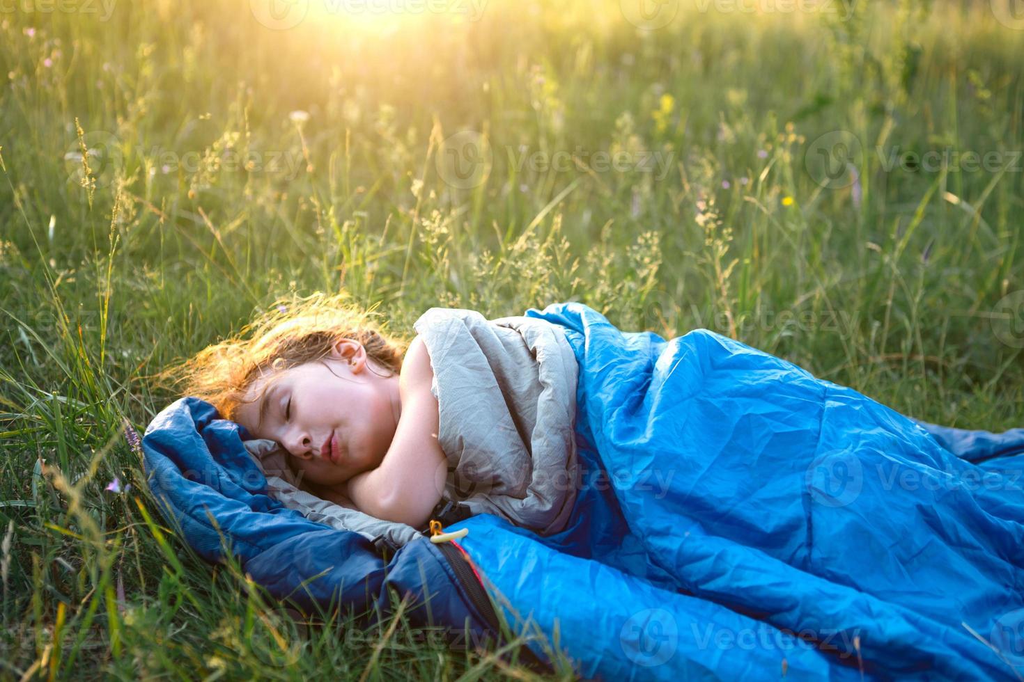 ein kind schläft in einem schlafsack auf dem gras bei einem campingausflug - umweltfreundliche erholung im freien, gesunder lebensstil, sommerzeit. süßen und friedlichen Schlaf. Mückenstiche, Abwehrmittel. foto