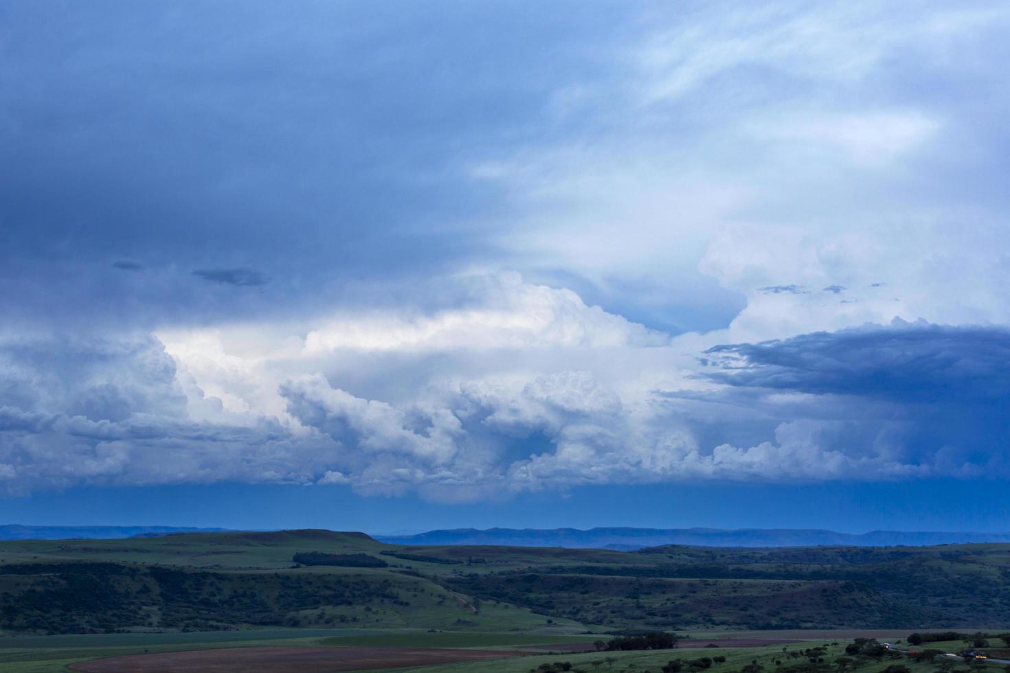 Blauer Himmel und weiße Kumuluswolken über grüner Landschaft nach Sonnenuntergang foto