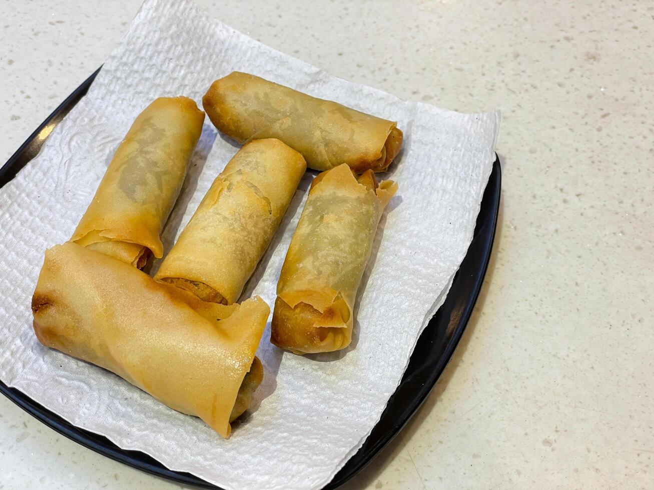 Gebratene Frühlingsrollen-Snacks werden auf einem schwarzen Teller arrangiert. von der oberen Ecke der Seite genommen. mit Gewebe beschichtet, um Öl zu absorbieren. foto