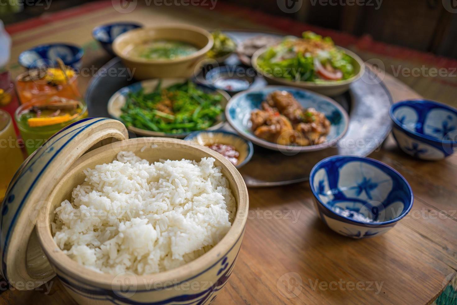 vietnamesisches familienkochset für vier personen gekochter reis, gemüsesuppe und gebratener fisch, gebratene zwiebeln mit hähnchen, gurkenscheibe, traditionelles vietnamesisches gericht auf dem land. foto