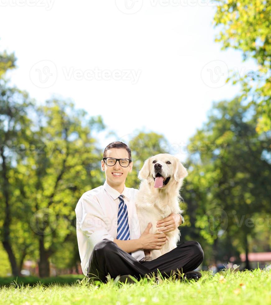 Mann sitzt auf einem Gras und umarmt seinen Labradorhund foto