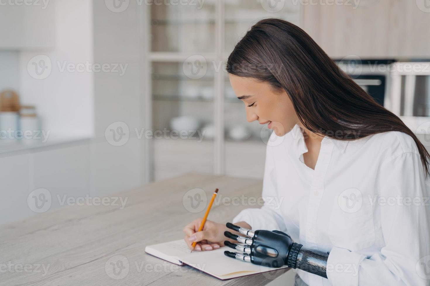 Schulmädchen mit bionischer Prothese studiert oder arbeitet aus der Ferne und macht sich Notizen am Schreibtisch. foto